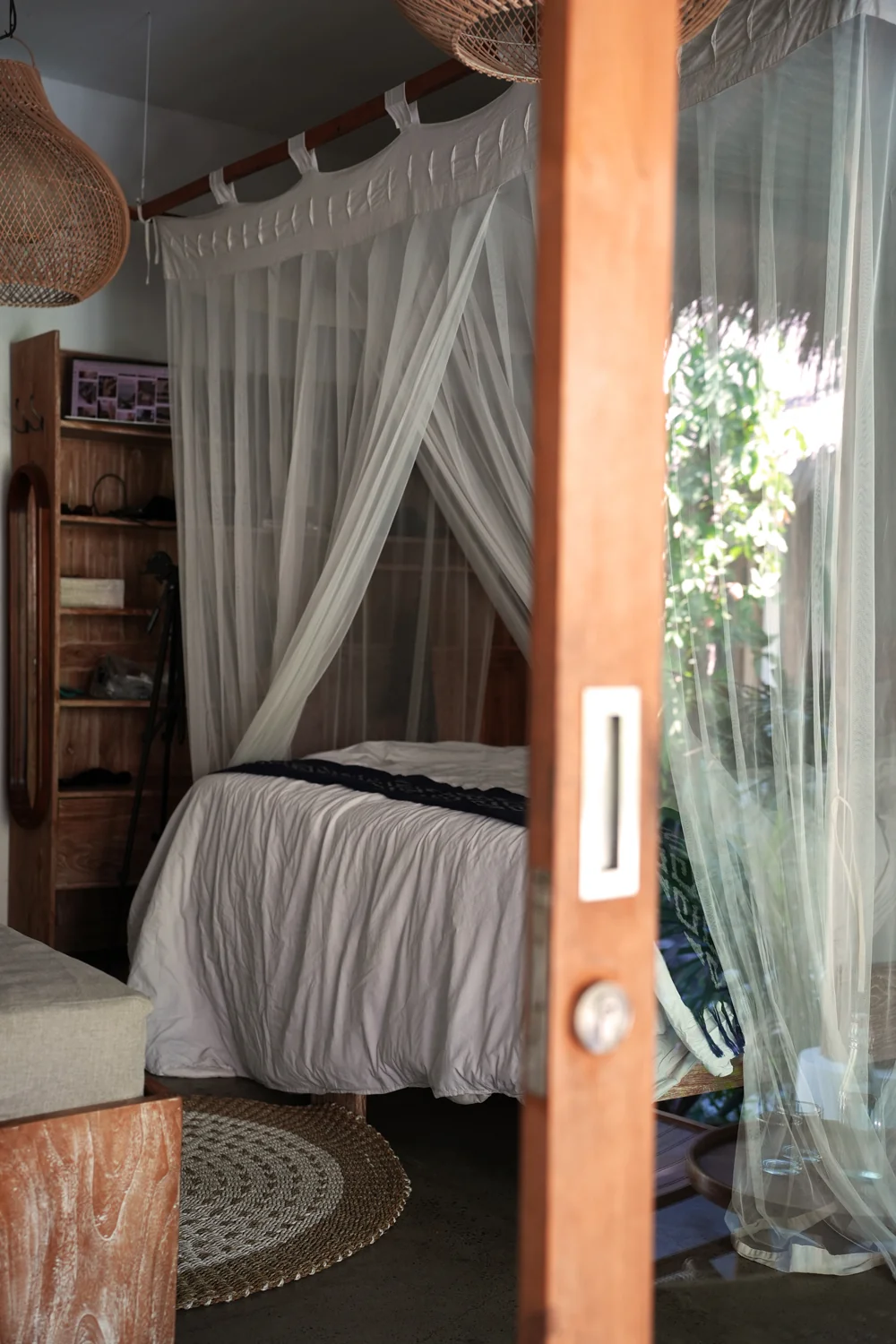 Bungalow bedroom with a canopy bed and sheer curtains, seen through an open timber door