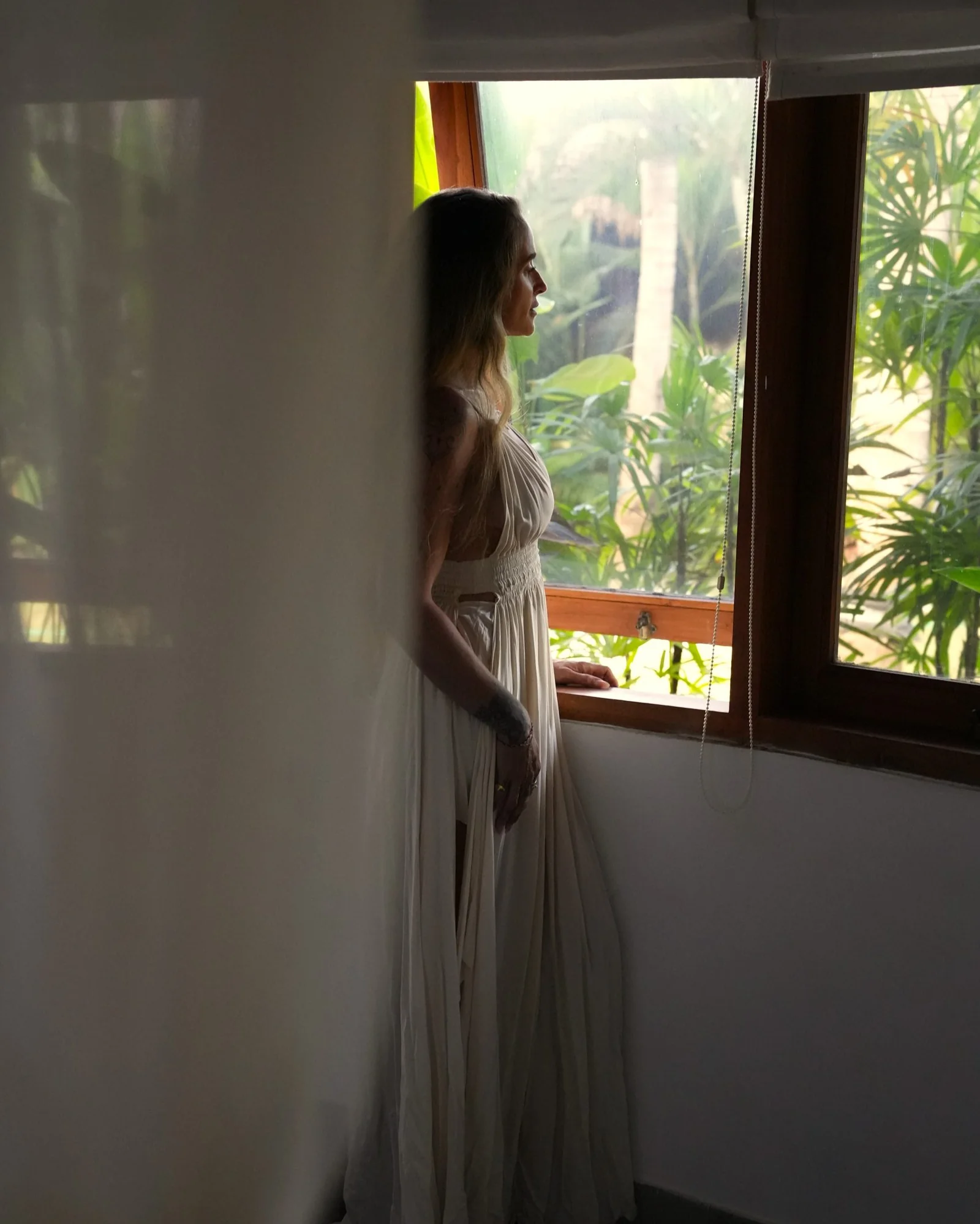Woman in a white dress looking out of a villa window