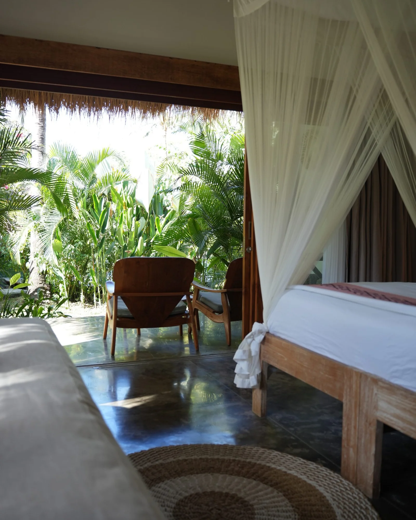 Canopy bed and timber chairs in a villa opening onto the garden