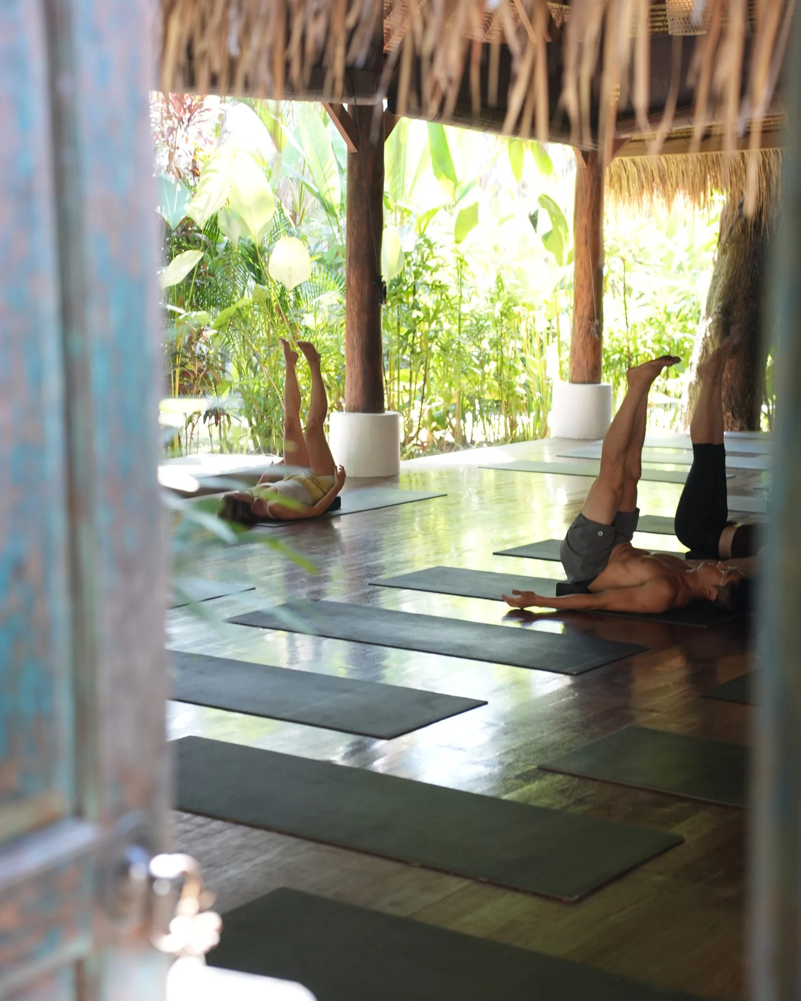 Yoga class with legs raised, framed by the shala doorway
