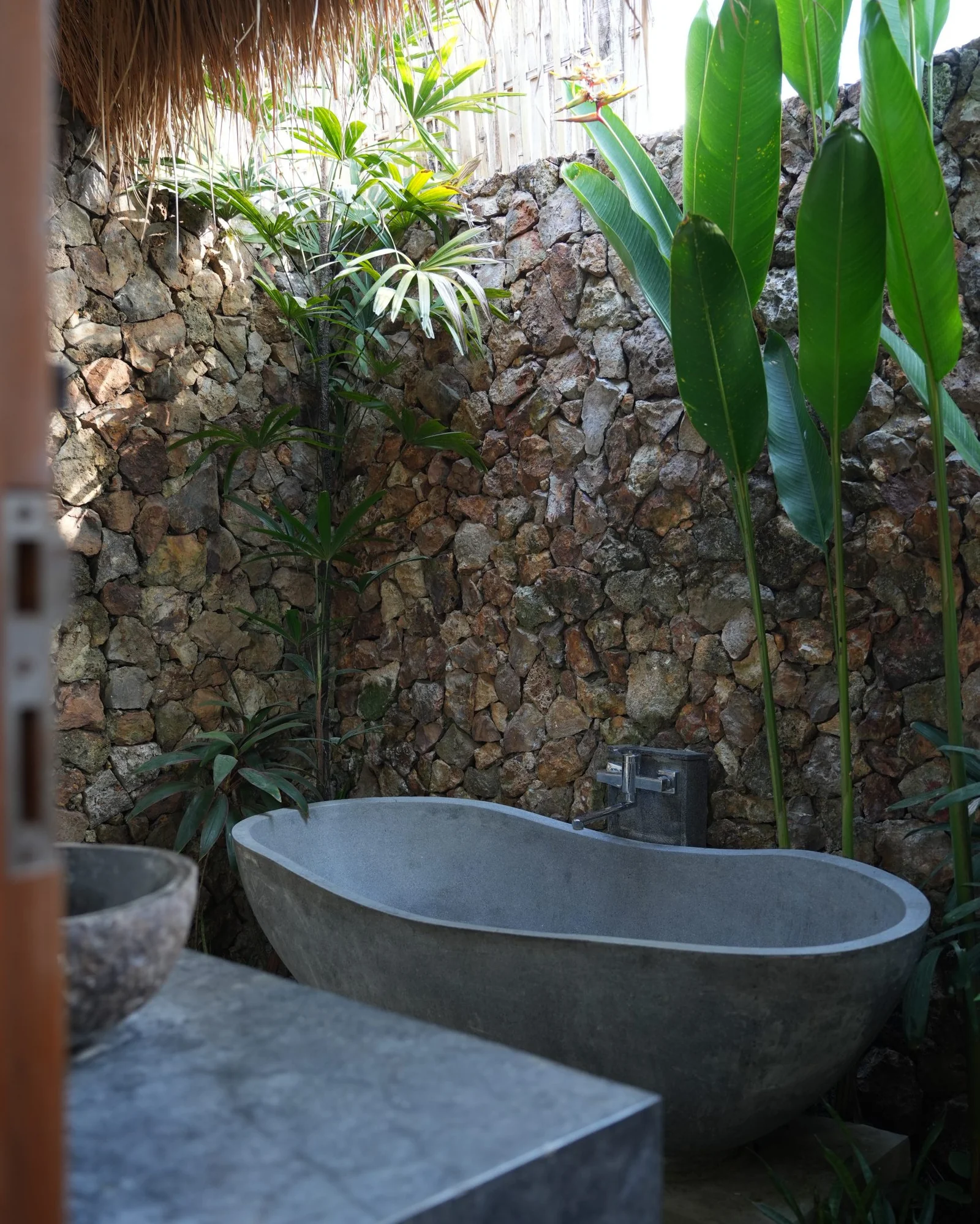Outdoor stone bathroom with a freestanding bath and tropical plants