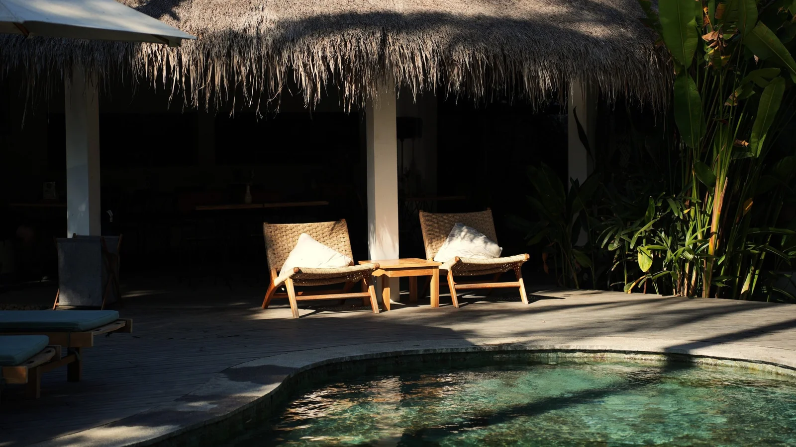 Pool and loungers beneath a thatched pavilion in late-afternoon light