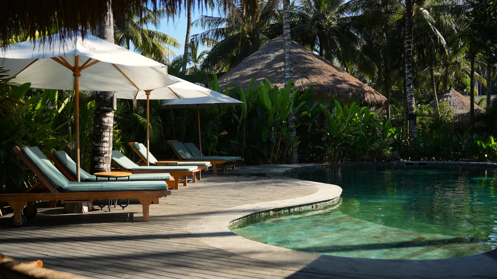 Pool deck with white umbrellas and sun loungers at Mana Eco Retreat