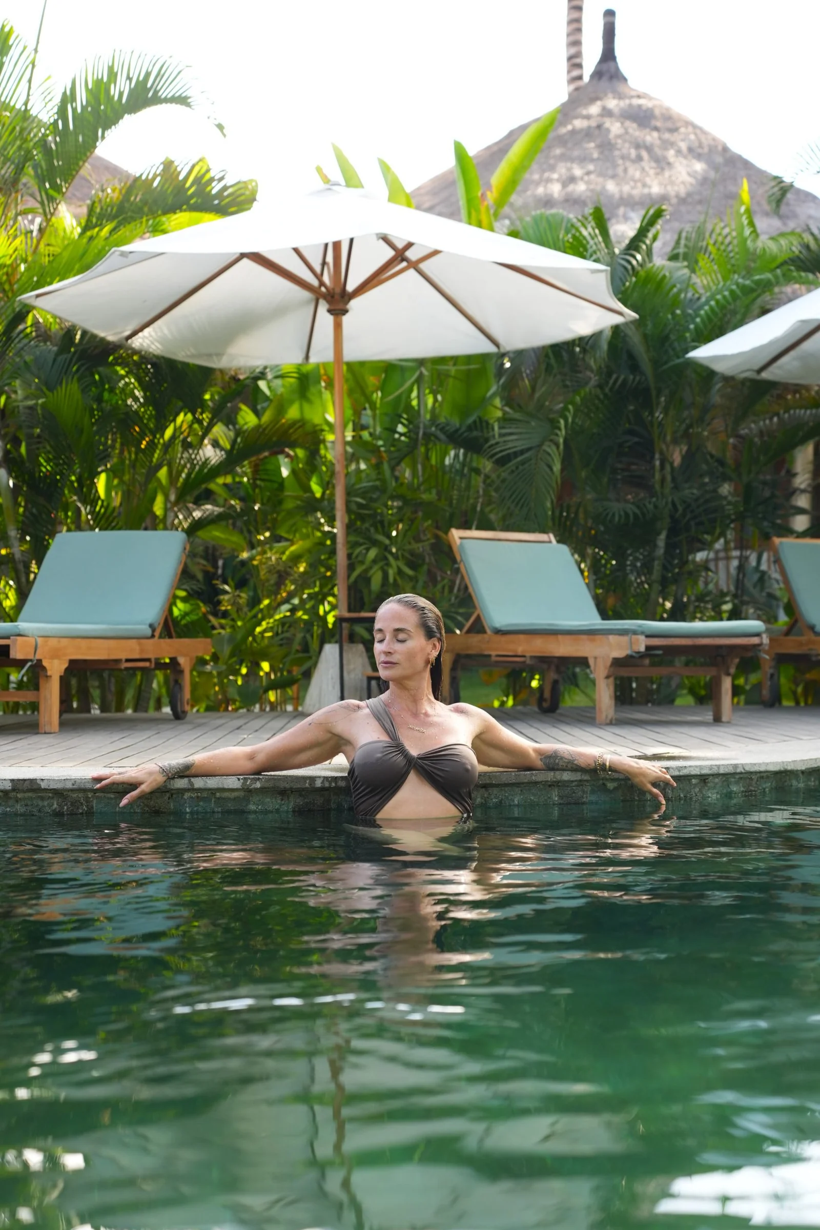 Woman resting at the edge of the pool beneath a white umbrella
