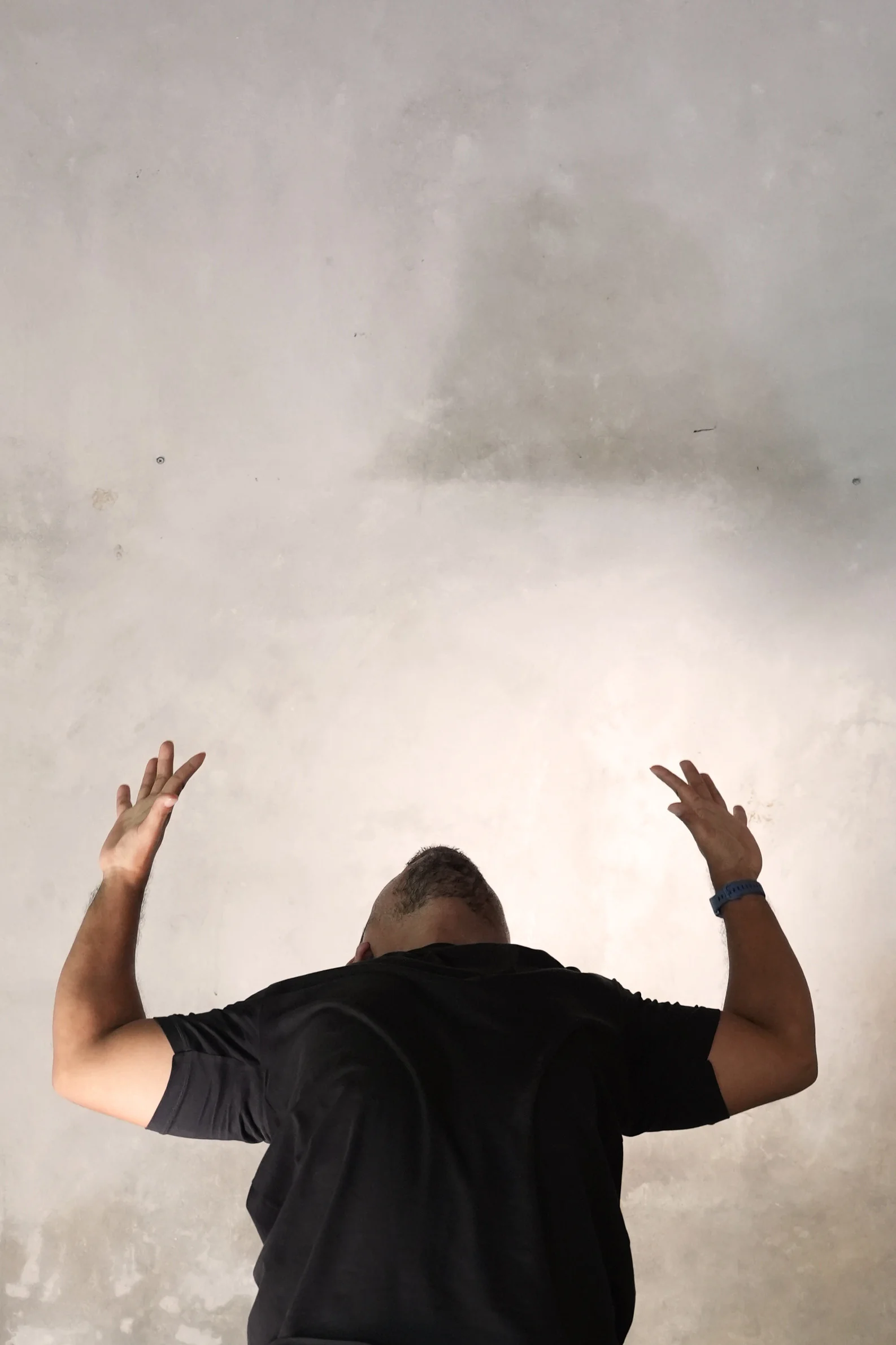 Man raising his arms in a yoga stretch against a pale concrete wall