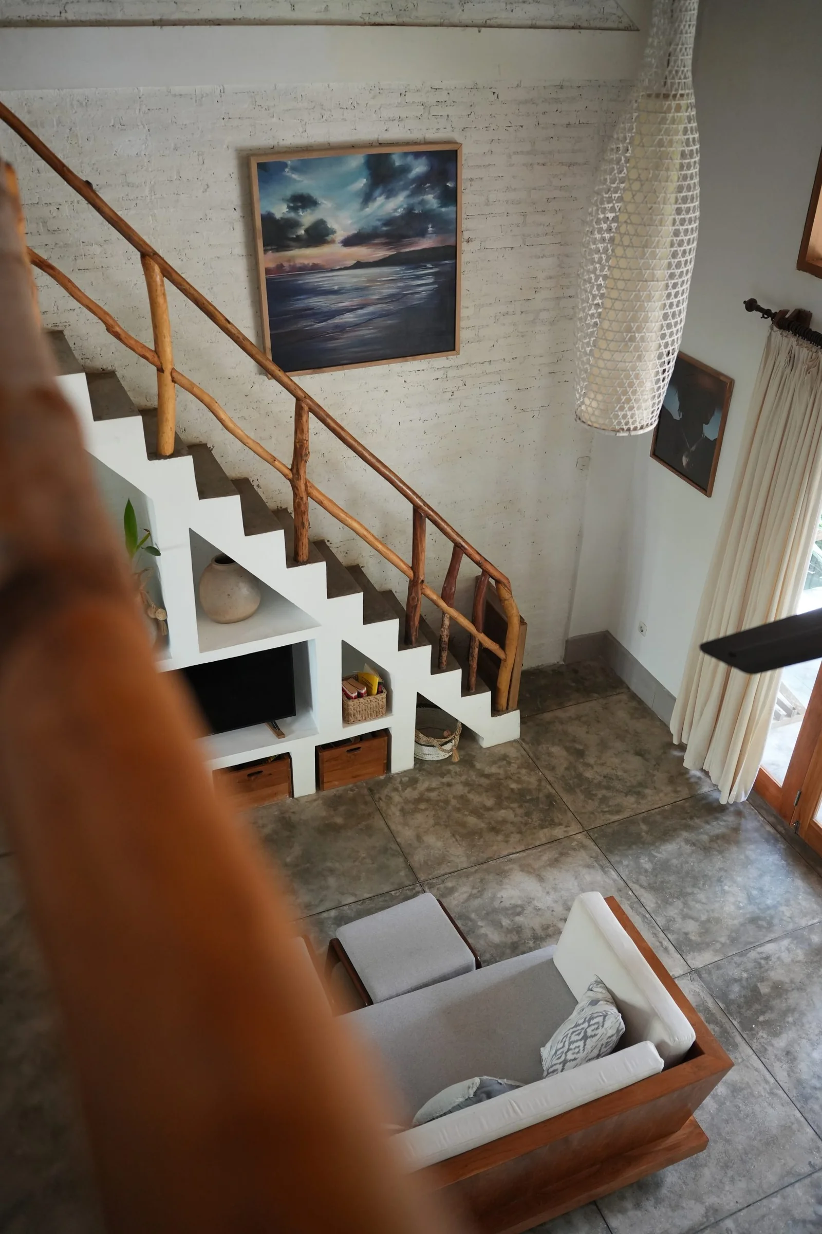Two-storey villa interior with a timber staircase and an ocean painting