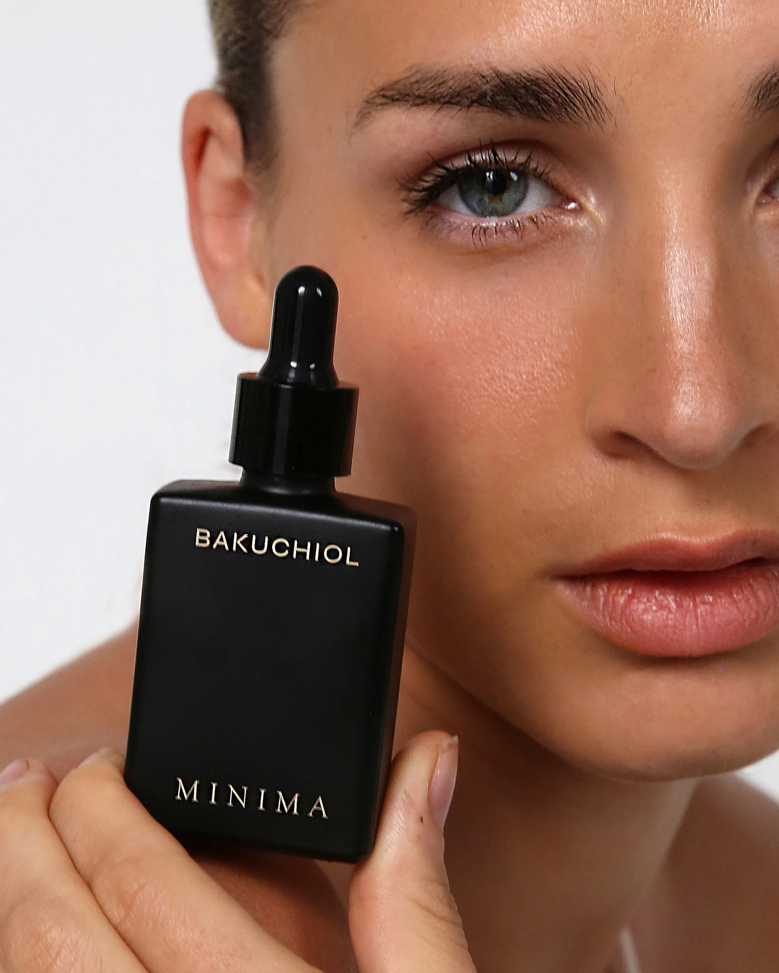 Model holding a Minima Bakuchiol bottle against her cheek