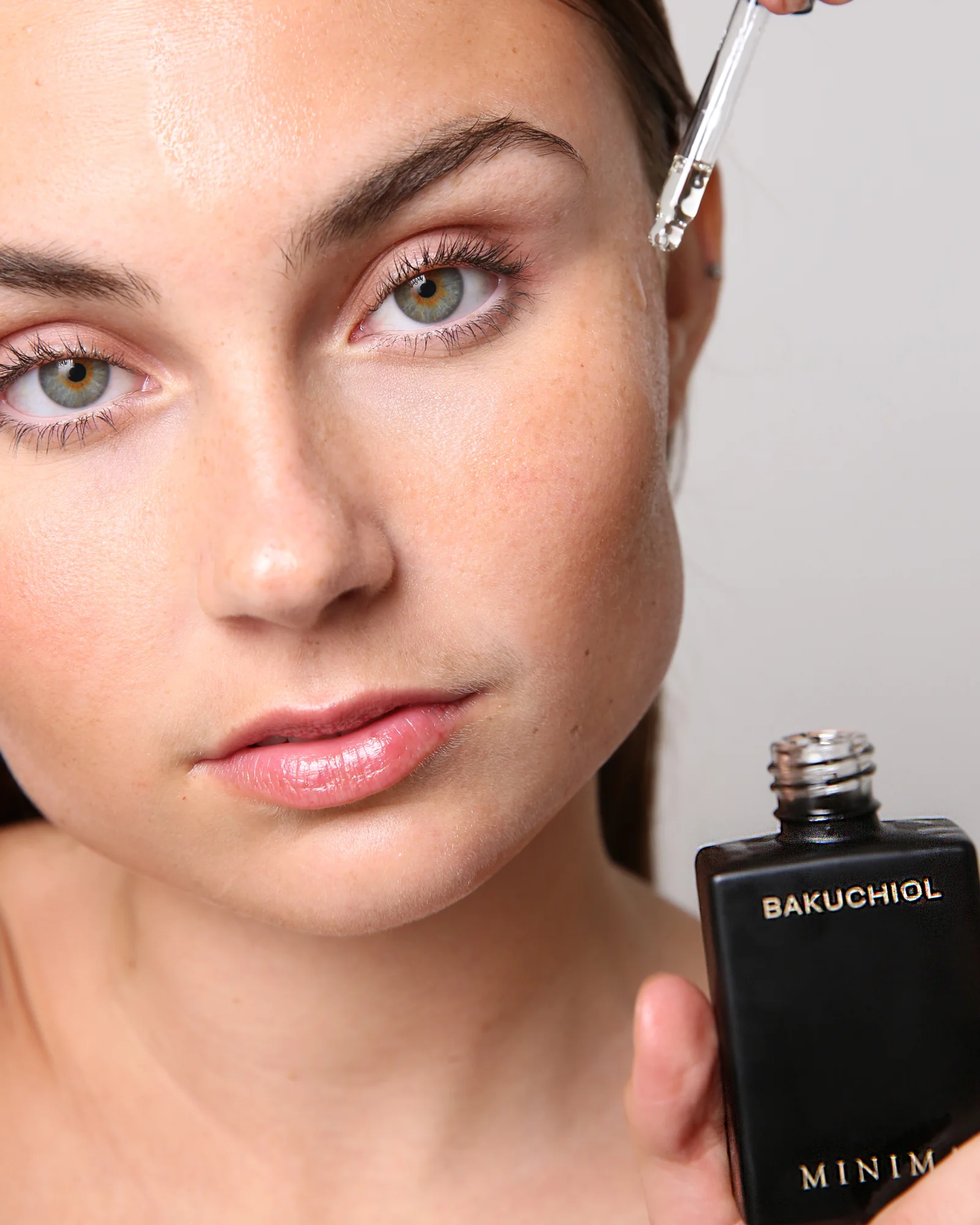 Model applying Minima Aesthetica Bakuchiol serum with a dropper