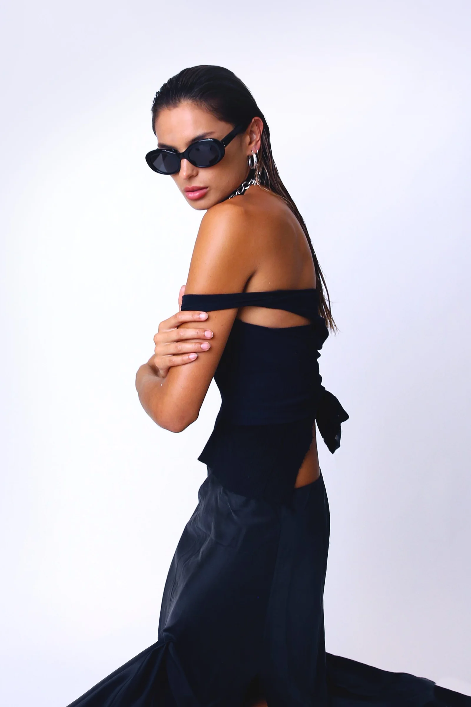Model in a black off-shoulder dress and sunglasses against a pale studio backdrop