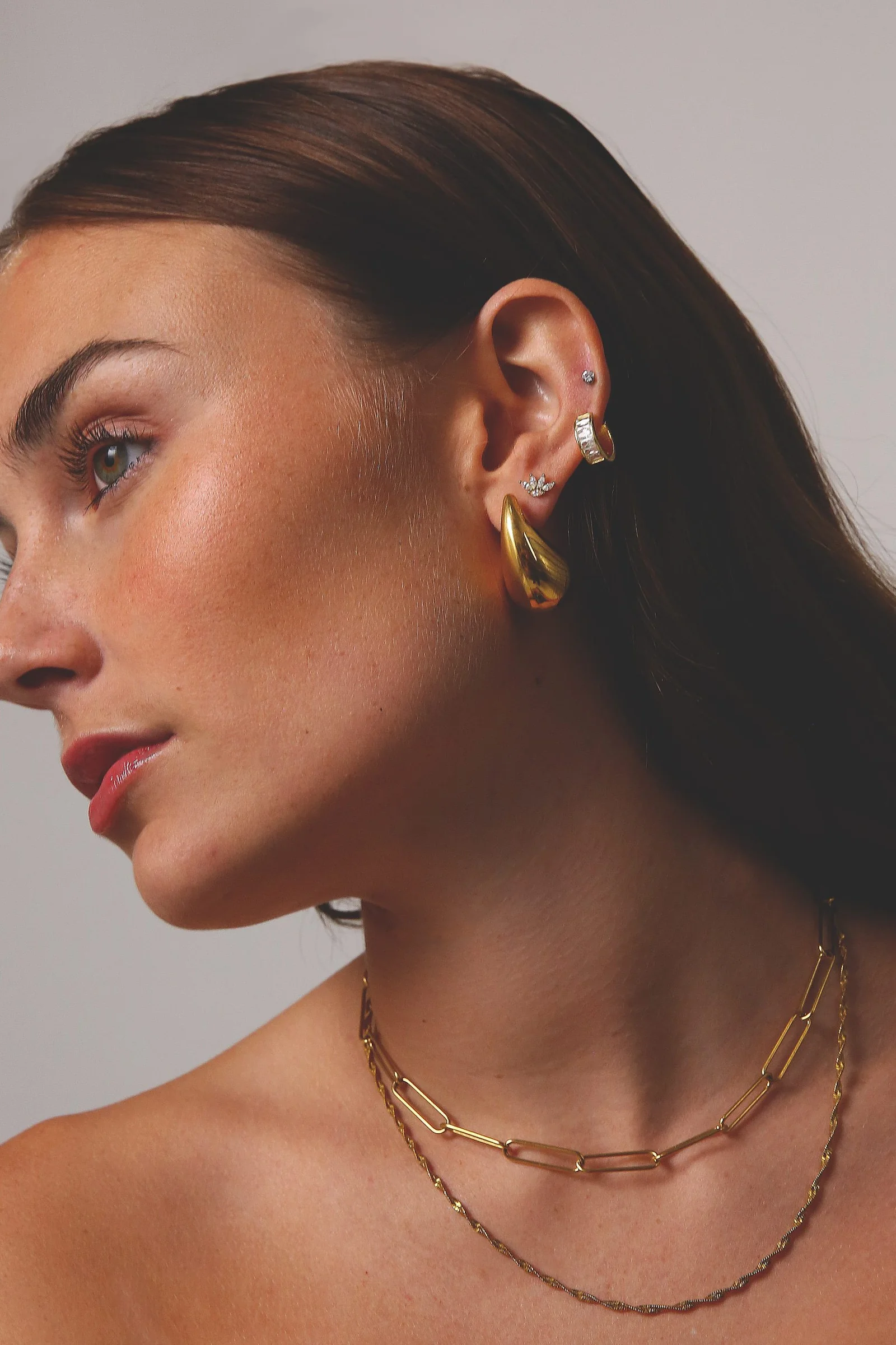 Model in profile wearing gold earrings and layered gold chains