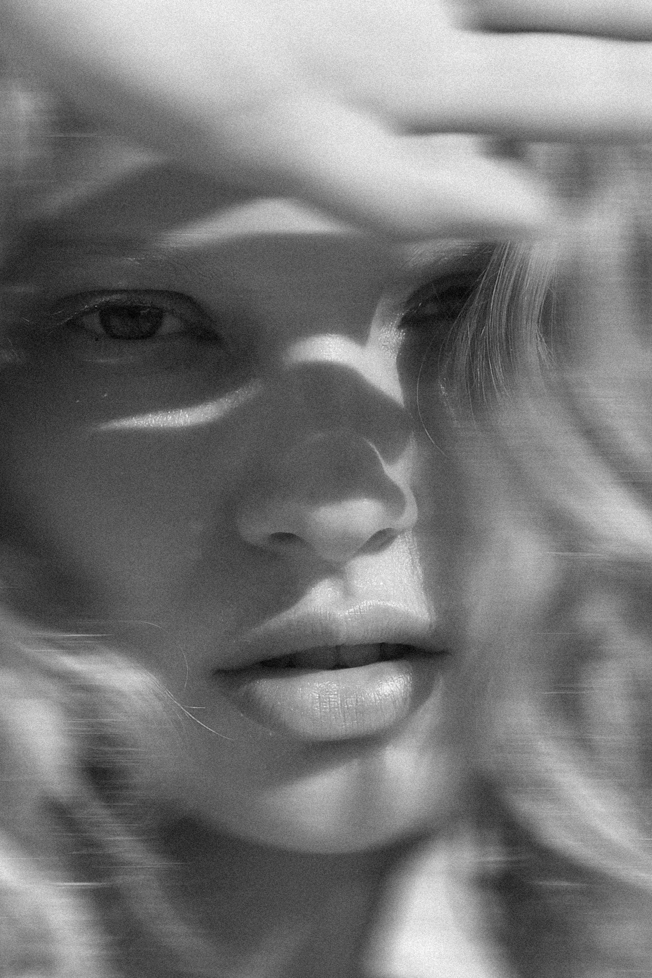 Black and white close-up of a face in shadow, a hand raised to the light