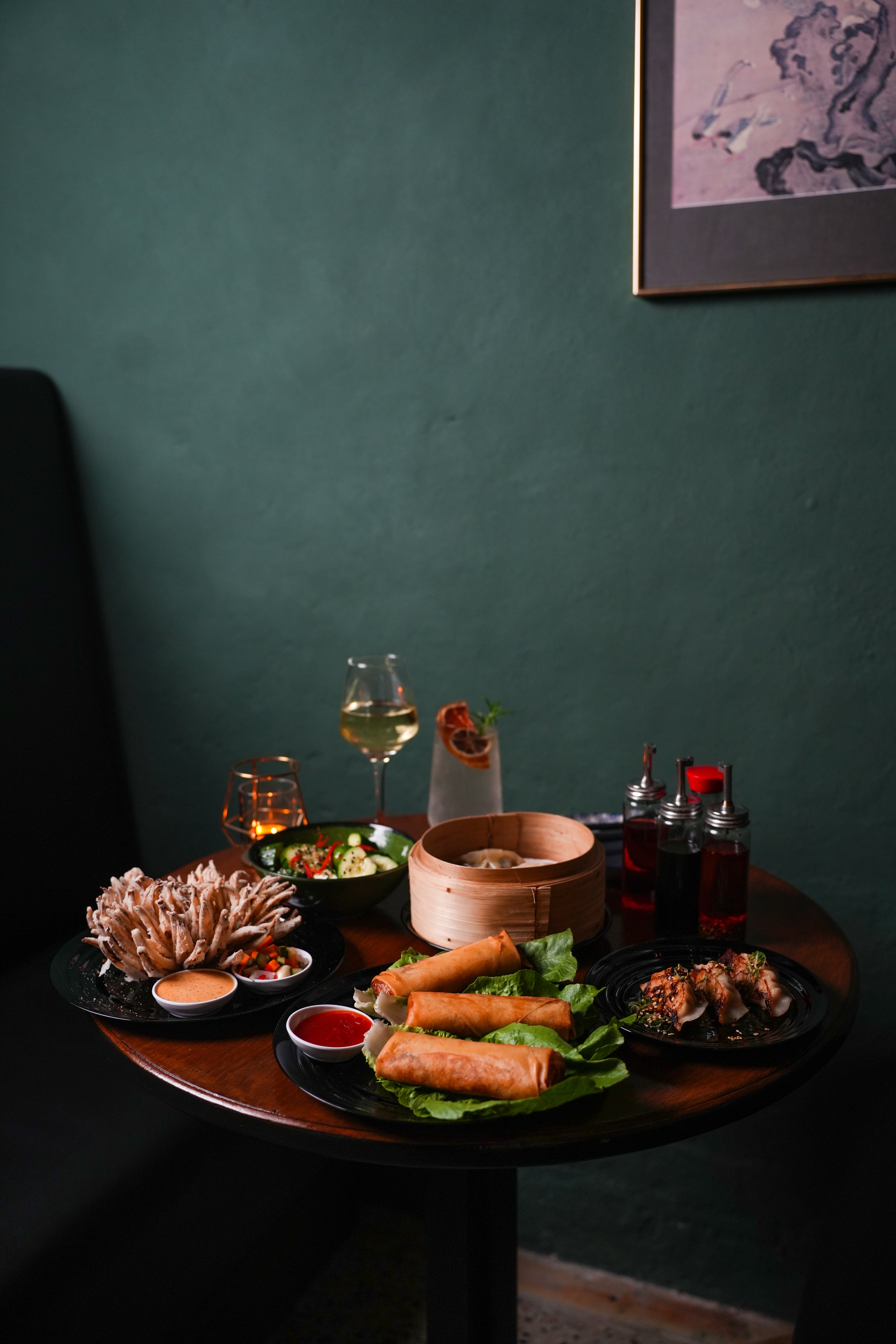 rESTAURANT Dinner table photography with plates of food, drinks, and a candle against a dark green wall.
