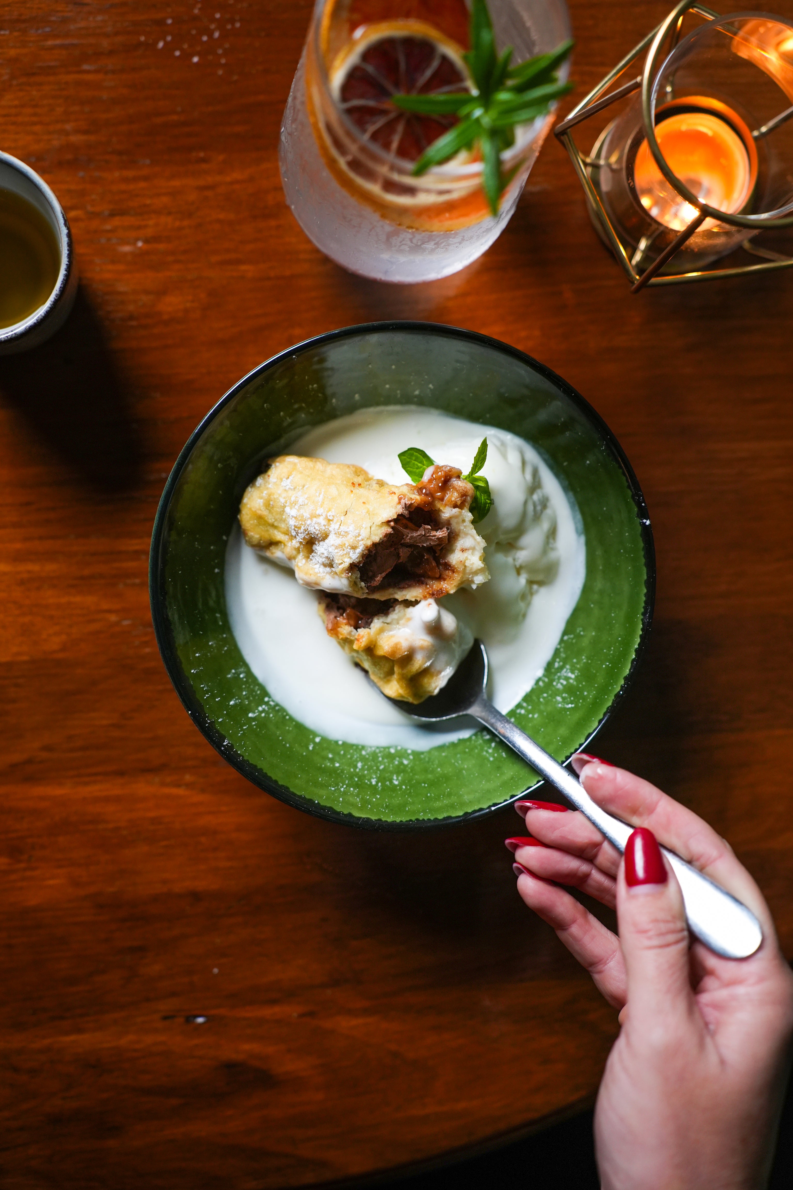 Green bowl with dessert on a wooden table with a hand holding a spoon.